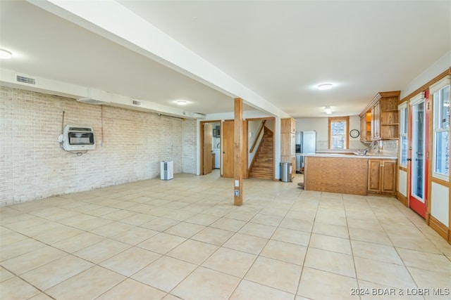 kitchen featuring white refrigerator, light tile patterned floors, kitchen peninsula, brick wall, and heating unit