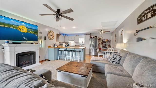 living room featuring ceiling fan, light colored carpet, and sink