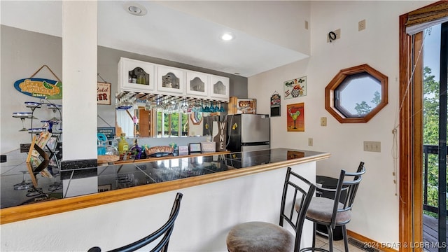 kitchen featuring stainless steel refrigerator, kitchen peninsula, white cabinets, and a breakfast bar