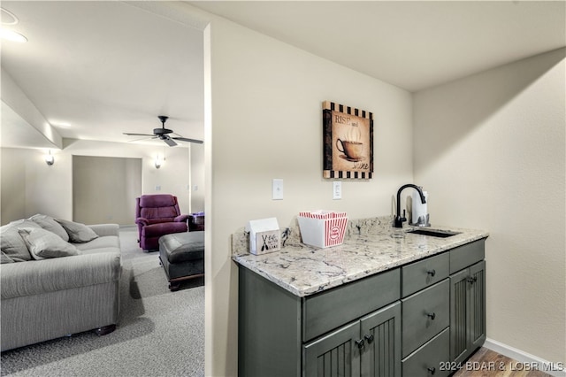 bar with ceiling fan, gray cabinets, light stone counters, and sink