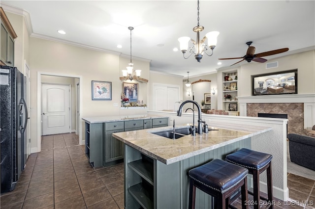 kitchen featuring black fridge with ice dispenser, built in shelves, a center island with sink, and hanging light fixtures