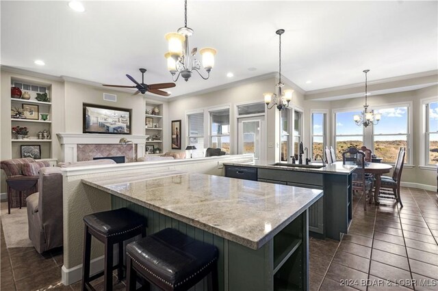 kitchen featuring pendant lighting, a center island, sink, built in shelves, and light stone counters