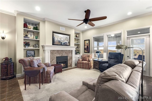 living room with a tiled fireplace, ceiling fan, built in features, and ornamental molding