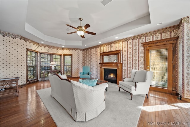 living room featuring hardwood / wood-style flooring, a raised ceiling, and ceiling fan