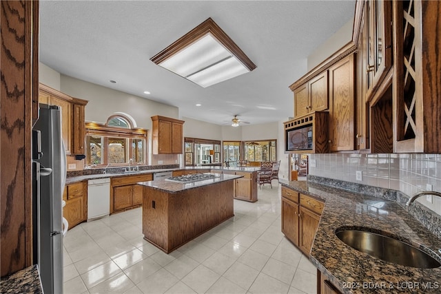 kitchen featuring backsplash, stainless steel appliances, sink, dark stone countertops, and a kitchen island