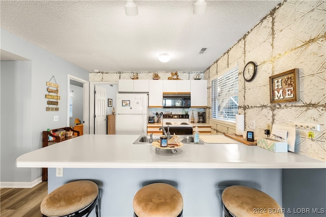 kitchen featuring white cabinets, a kitchen bar, white appliances, and hardwood / wood-style flooring