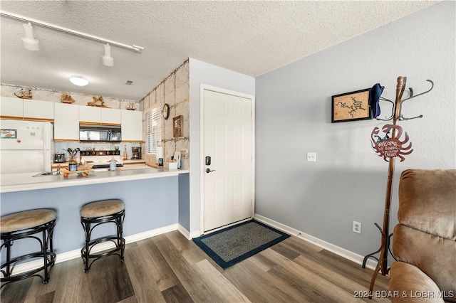 6005 Baydy Peak Rd Unit 102, Osage Beach, MO 65065 - kitchen with black microwave, freestanding refrigerator, dark wood-style flooring, a kitchen bar, and a textured ceiling