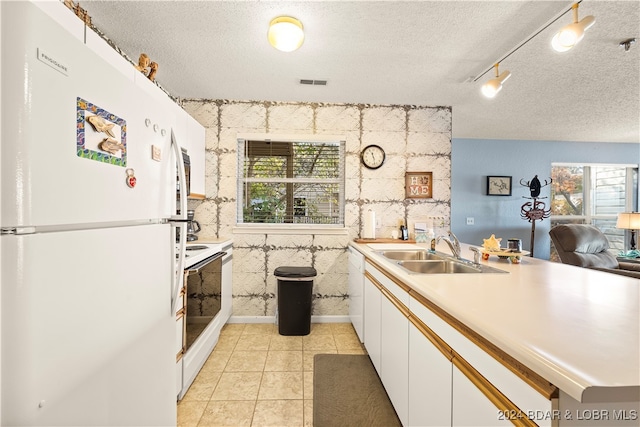 kitchen featuring a textured ceiling, white appliances, sink, light tile patterned floors, and white cabinetry