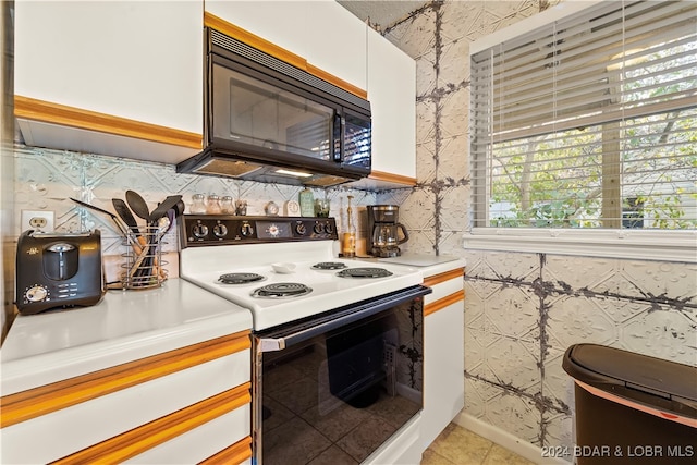 kitchen with white electric range oven, light tile patterned floors, and white cabinets