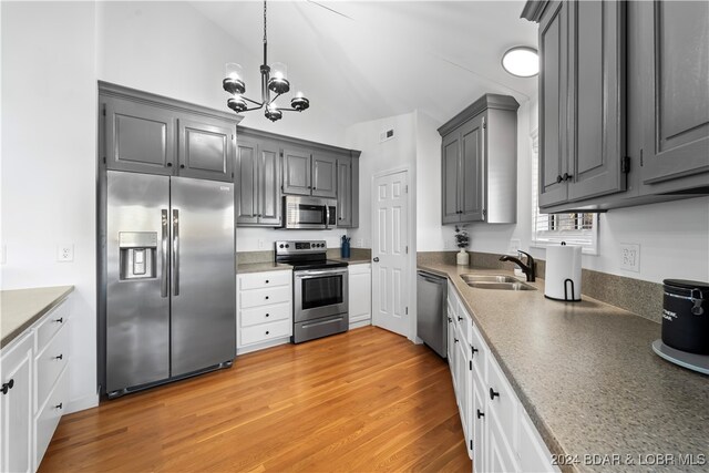 kitchen with gray cabinetry, sink, stainless steel appliances, lofted ceiling, and light wood-type flooring