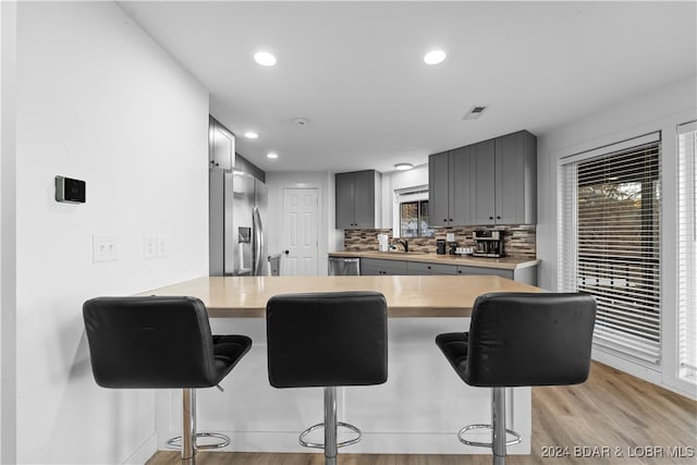 kitchen with gray cabinetry, a kitchen breakfast bar, light hardwood / wood-style floors, kitchen peninsula, and stainless steel appliances