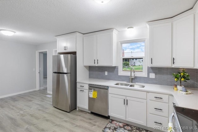 kitchen featuring light wood finished floors, decorative backsplash, white cabinets, appliances with stainless steel finishes, and a sink