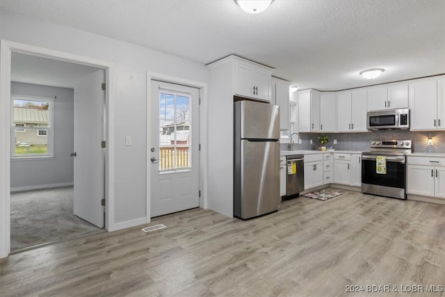 kitchen with appliances with stainless steel finishes, light countertops, light wood-style flooring, and backsplash