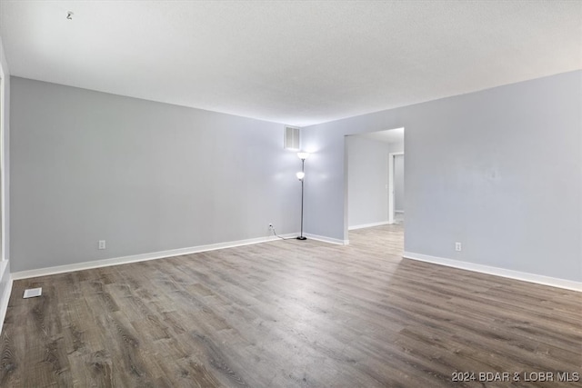 empty room featuring wood finished floors, visible vents, and baseboards