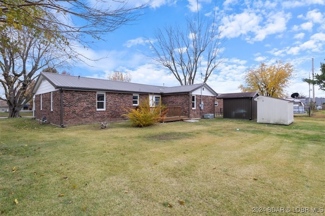 rear view of property featuring a deck, brick siding, an outdoor structure, a lawn, and a shed