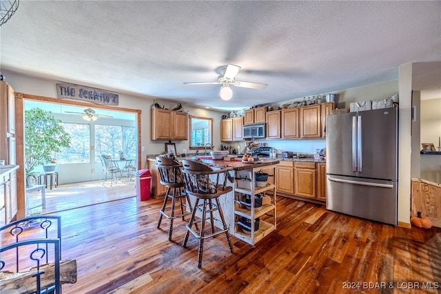 kitchen featuring dark wood-type flooring, ceiling fan, a textured ceiling, a kitchen bar, and stainless steel appliances