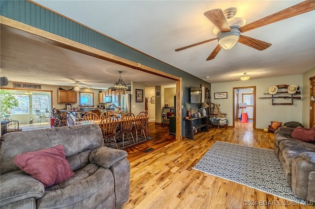 living room with a textured ceiling, ceiling fan with notable chandelier, and light wood-type flooring