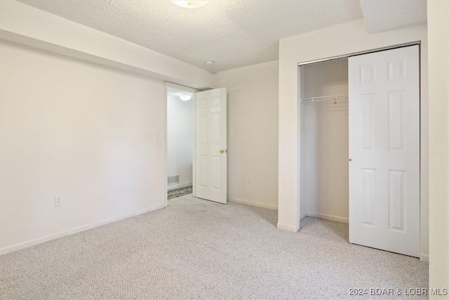 unfurnished bedroom with light carpet, a textured ceiling, and a closet