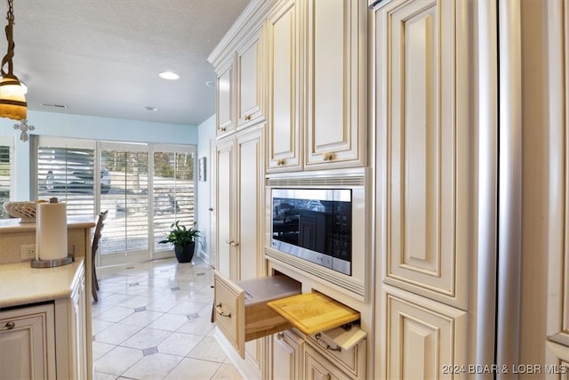 kitchen with stainless steel microwave, light tile patterned flooring, a textured ceiling, and cream cabinetry