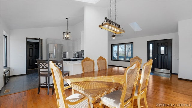 dining room with dark hardwood / wood-style flooring and vaulted ceiling with skylight