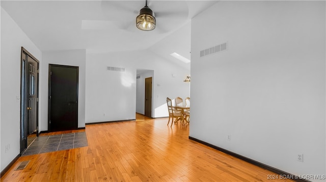 empty room featuring ceiling fan, vaulted ceiling with skylight, and light wood-type flooring