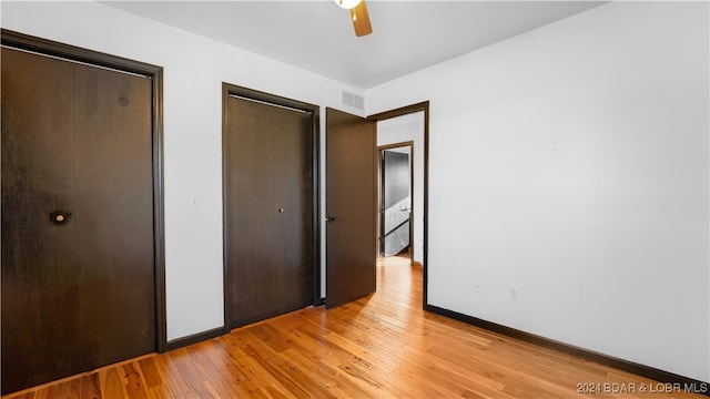 unfurnished bedroom featuring ceiling fan, two closets, and light wood-type flooring