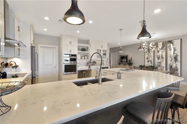 kitchen featuring stainless steel double oven, sink, white cabinets, and pendant lighting