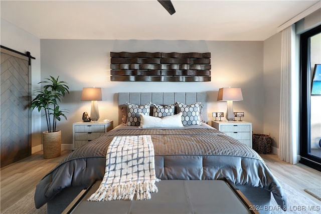 bedroom featuring a barn door, ceiling fan, and light hardwood / wood-style flooring