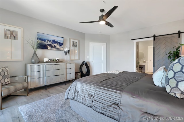 bedroom featuring a barn door, light hardwood / wood-style floors, ceiling fan, and ensuite bathroom