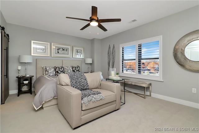 bedroom with ceiling fan, a barn door, and light carpet