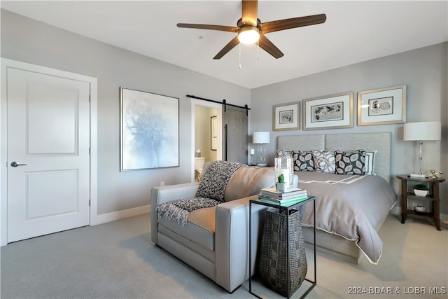 carpeted bedroom with a barn door, ceiling fan, and ensuite bath