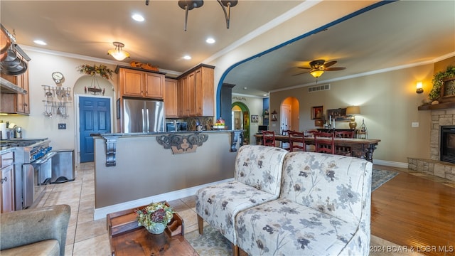 kitchen with crown molding, ceiling fan, stainless steel appliances, a fireplace, and backsplash