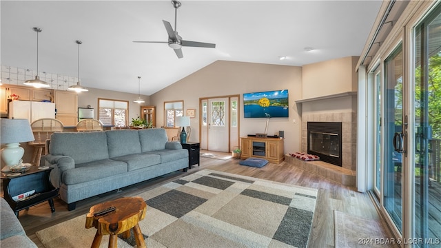 living room featuring ceiling fan, a fireplace, vaulted ceiling, and light wood-type flooring