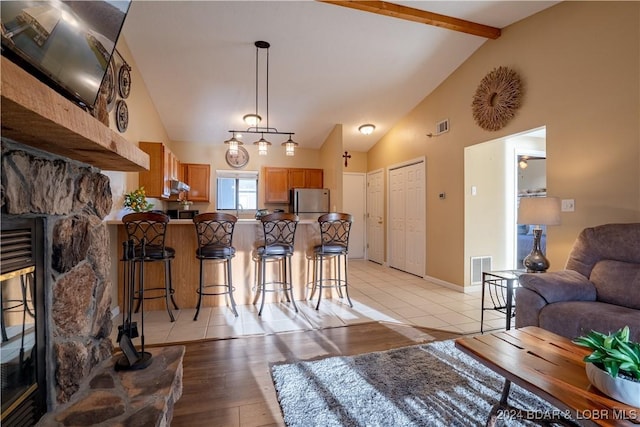 kitchen featuring brown cabinetry, beamed ceiling, a peninsula, freestanding refrigerator, and a kitchen breakfast bar