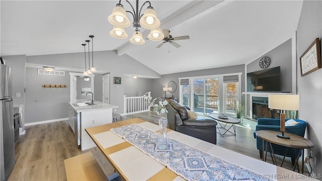 dining area featuring vaulted ceiling with beams, sink, light hardwood / wood-style floors, and ceiling fan with notable chandelier