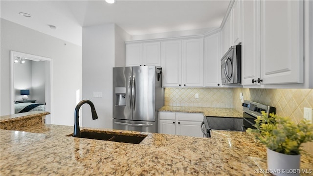 kitchen featuring light stone countertops, backsplash, stainless steel appliances, sink, and white cabinets