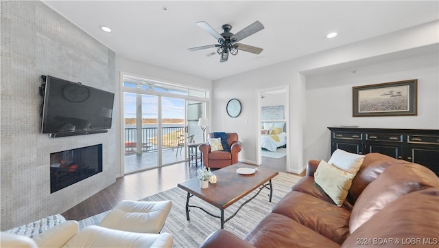 living room with hardwood / wood-style flooring, ceiling fan, and a large fireplace