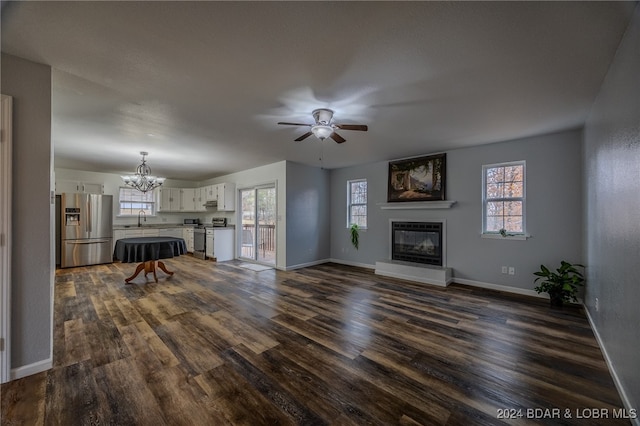 unfurnished living room with ceiling fan with notable chandelier, dark hardwood / wood-style flooring, a wealth of natural light, and sink