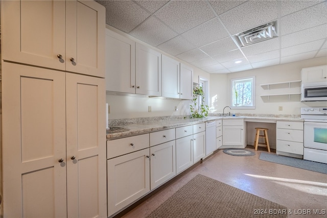 kitchen featuring white cabinetry, sink, light stone counters, white appliances, and a paneled ceiling