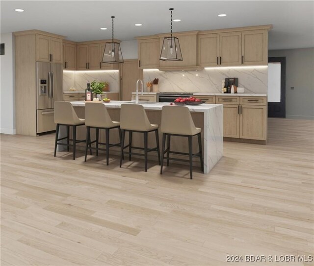 kitchen featuring appliances with stainless steel finishes, a center island with sink, light hardwood / wood-style floors, and decorative light fixtures