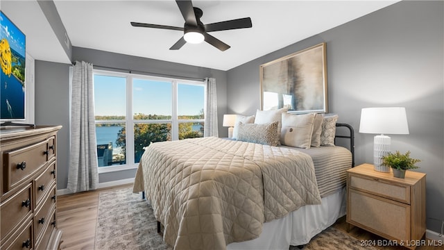 bedroom featuring ceiling fan, a water view, and light hardwood / wood-style floors