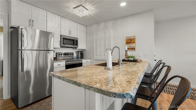 kitchen with a kitchen bar, appliances with stainless steel finishes, sink, white cabinets, and hardwood / wood-style floors