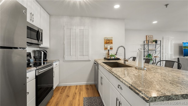 kitchen with light wood-type flooring, light stone counters, stainless steel appliances, sink, and white cabinetry