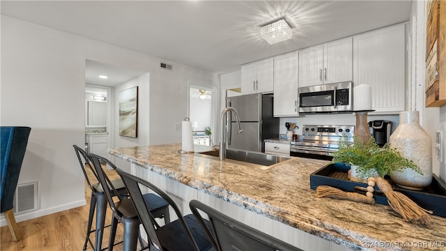 kitchen featuring light stone countertops, appliances with stainless steel finishes, sink, white cabinets, and light hardwood / wood-style floors