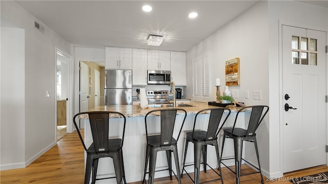 kitchen with light stone countertops, kitchen peninsula, light hardwood / wood-style floors, white cabinets, and appliances with stainless steel finishes