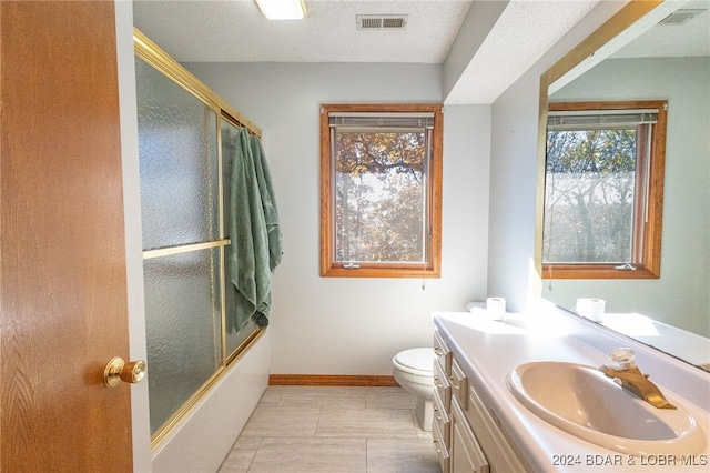 full bathroom with vanity, toilet, combined bath / shower with glass door, and a textured ceiling