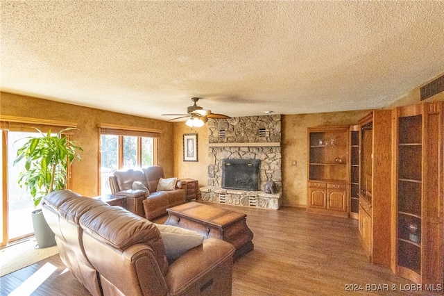 living room with a stone fireplace, ceiling fan, hardwood / wood-style floors, and a textured ceiling