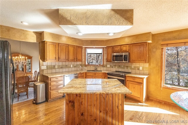 kitchen with appliances with stainless steel finishes, a textured ceiling, sink, light hardwood / wood-style flooring, and an inviting chandelier