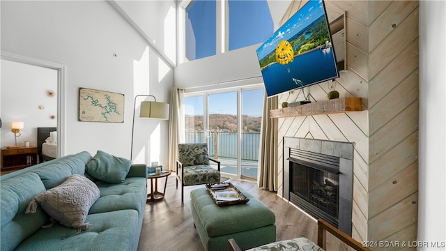 living room featuring a tiled fireplace, a towering ceiling, and hardwood / wood-style flooring