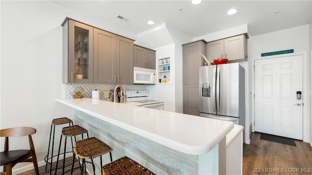 kitchen featuring a kitchen breakfast bar, kitchen peninsula, dark wood-type flooring, and white appliances